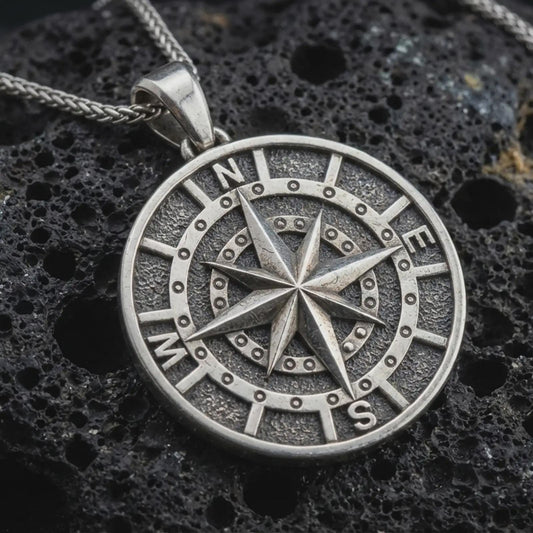 Sterling silver compass pendant necklace with an oxidized finish resting on textured volcanic rock, captured in a close-up premium studio composition.