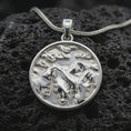 Load image into Gallery viewer, Polished silver mountain landscape pendant necklace displayed on black volcanic rock, shown in a refined macro product shot with layered peaks, pine tree silhouettes, and cloud relief.
