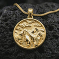 Load image into Gallery viewer, Gold plated mountain landscape pendant necklace presented on porous volcanic rock, highlighting the round nature-inspired design in a luxurious close-up jewelry image.
