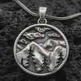 Load image into Gallery viewer, Sterling silver mountain landscape pendant necklace with an oxidized finish resting on textured volcanic rock, captured in a close-up premium studio composition.
