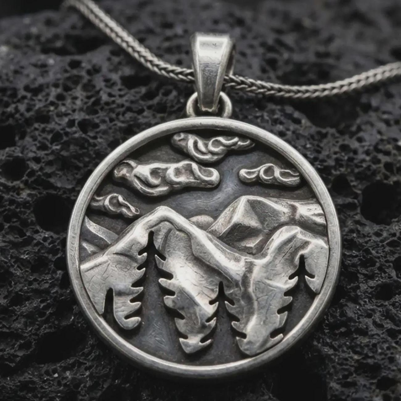 Sterling silver mountain landscape pendant necklace with an oxidized finish resting on textured volcanic rock, captured in a close-up premium studio composition.