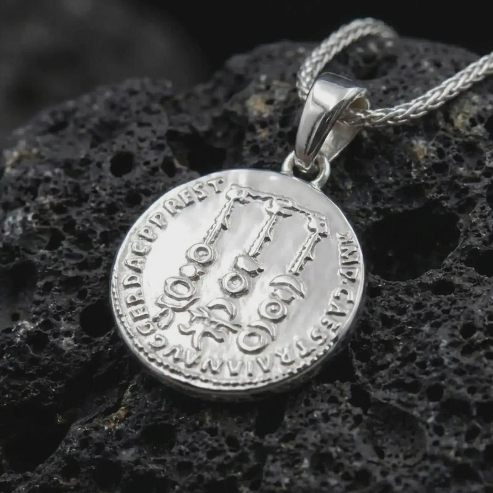 Polished silver Tiberius coin pendant necklace displayed on dark volcanic rock, shown in a premium close-up image that highlights the classical Roman portrait and historical coin medallion design.