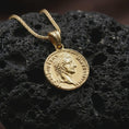 Load image into Gallery viewer, Gold plated Tiberius coin pendant necklace photographed on porous black volcanic stone, emphasizing the imperial side-profile relief and engraved ancient Roman lettering in a luxury jewelry composition.
