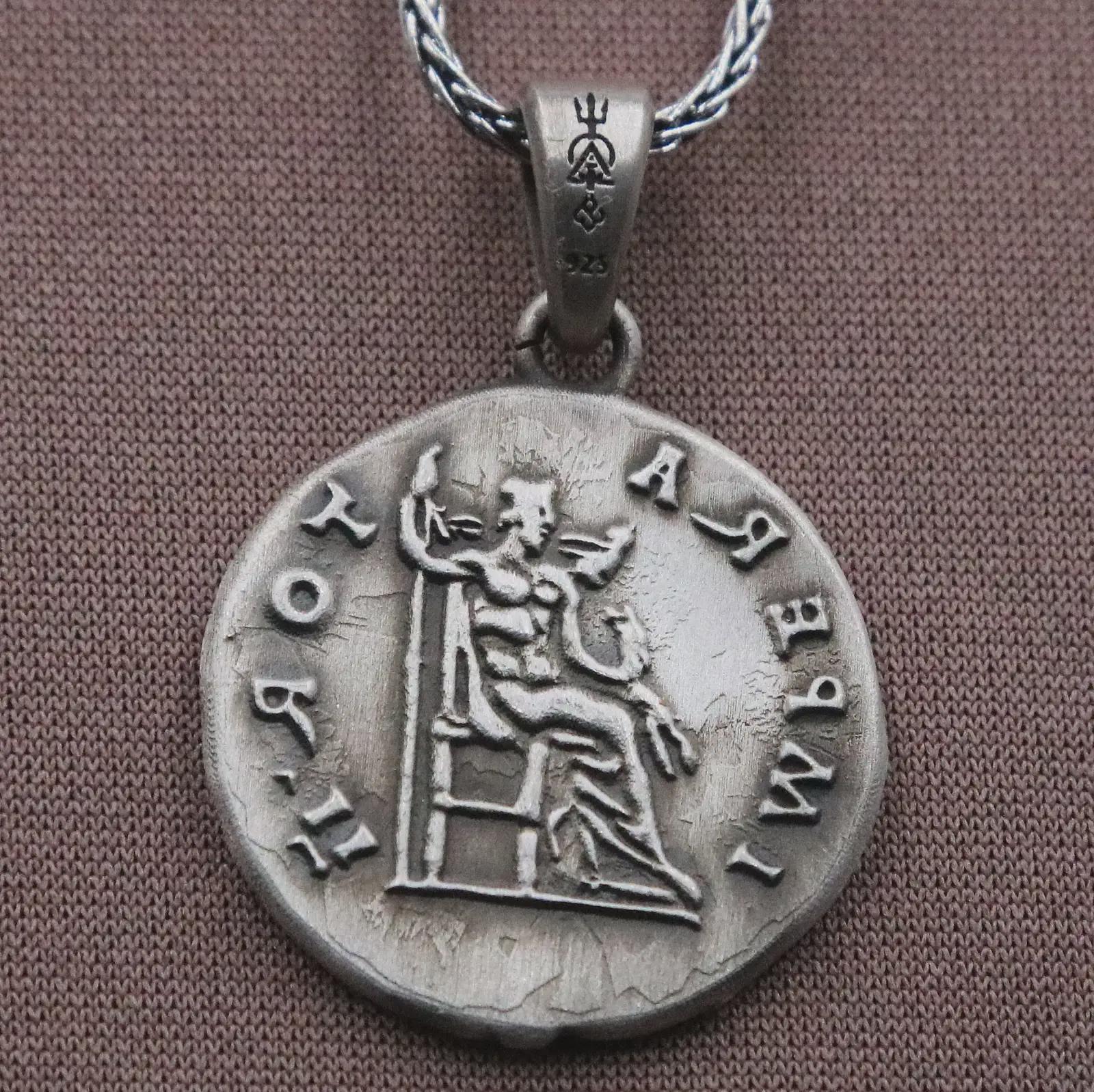 Oxidized Roman emperor coin pendant necklace resting on black volcanic stone, featuring a side profile imperial bust and antique Latin inscription in a detailed macro product photograph.