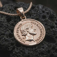 Load image into Gallery viewer, Rose gold plated Roman coin pendant necklace presented on textured volcanic stone, showcasing the round ancient medallion silhouette and detailed emperor bust in a refined macro studio shot.
