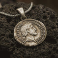 Load image into Gallery viewer, Bronze Roman emperor coin pendant necklace resting on black volcanic stone, featuring a side profile imperial bust and antique Latin inscription in a detailed macro product photograph.
