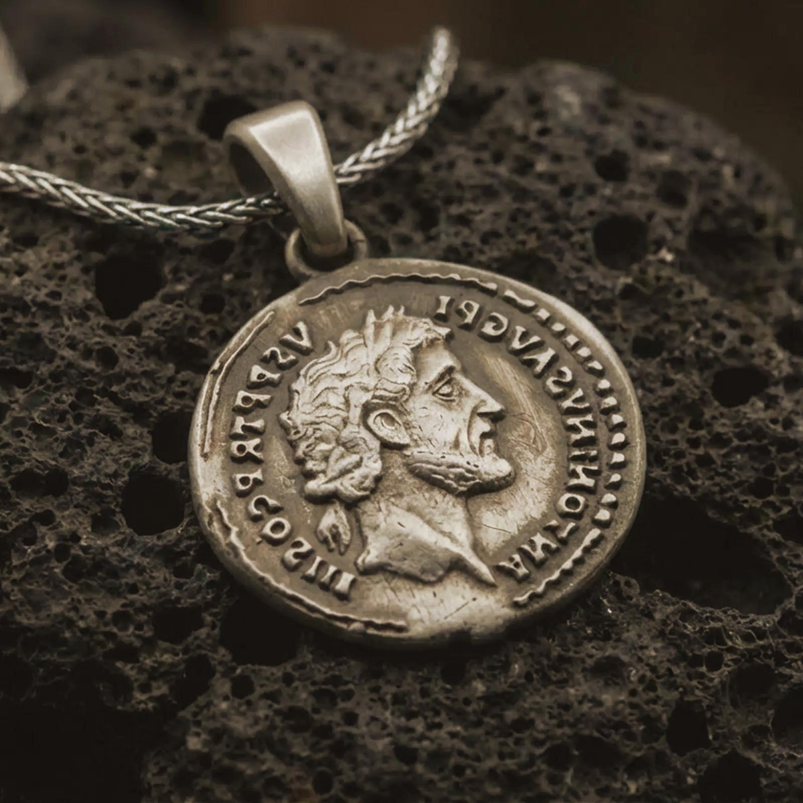 Bronze Roman emperor coin pendant necklace resting on black volcanic stone, featuring a side profile imperial bust and antique Latin inscription in a detailed macro product photograph.