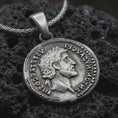 Load image into Gallery viewer, Oxidized Roman emperor coin pendant necklace resting on black volcanic stone, featuring a side profile imperial bust and antique Latin inscription in a detailed macro product photograph.
