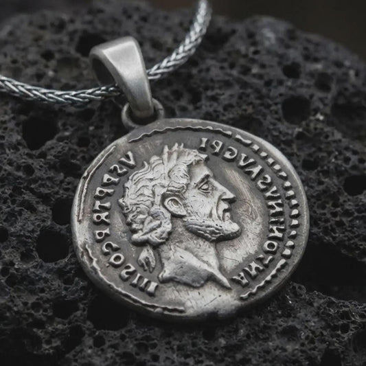 Oxidized Roman emperor coin pendant necklace resting on black volcanic stone, featuring a side profile imperial bust and antique Latin inscription in a detailed macro product photograph.
