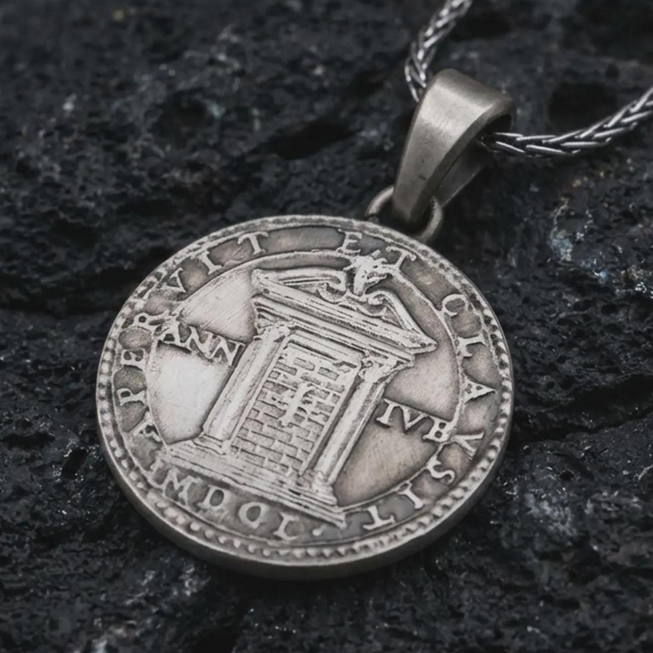 Oxidized Pope Innocent coin pendant necklace resting on black volcanic stone, featuring a papal portrait with Latin inscription in a detailed antique coin-style macro photograph.