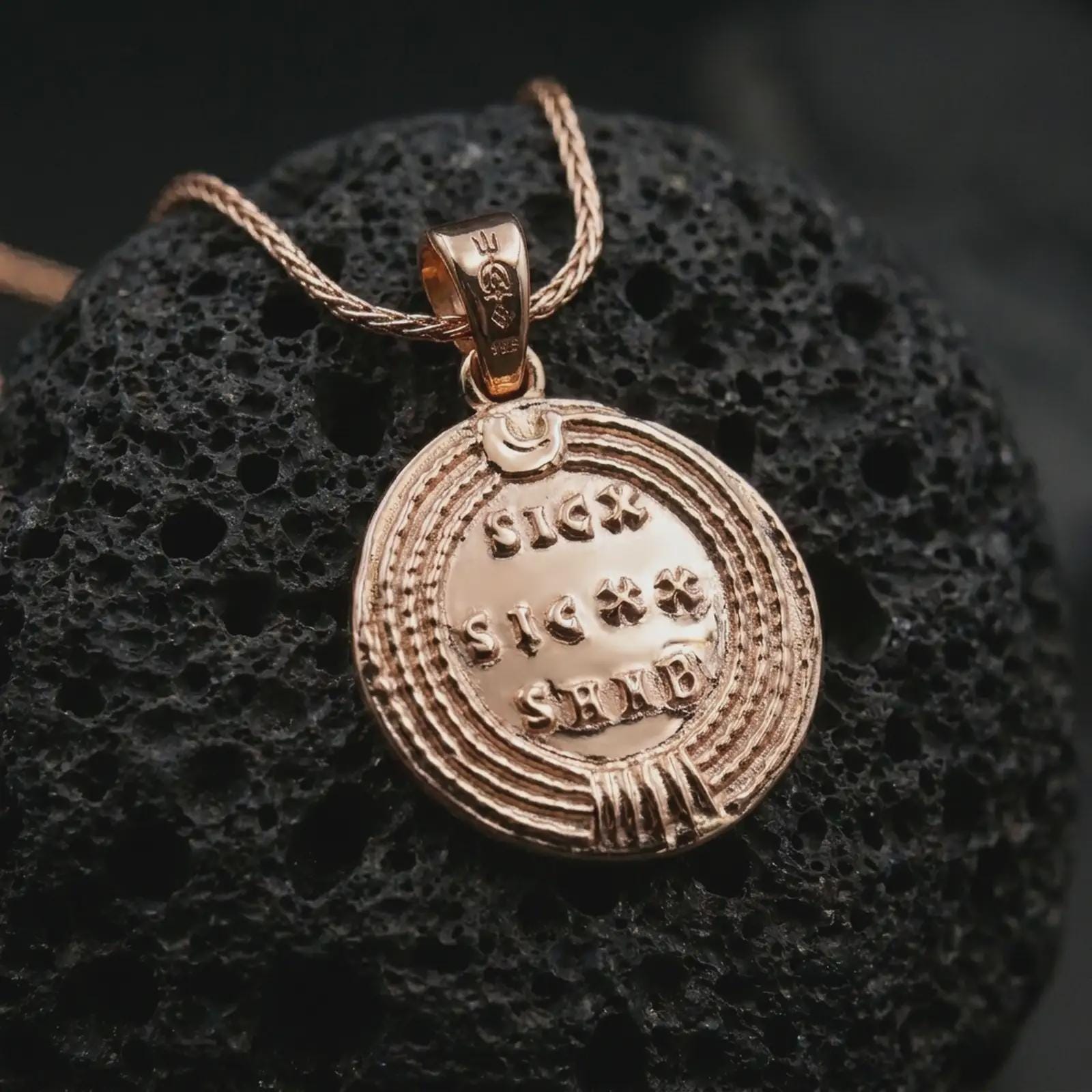 Rose gold plated Emperor Constans coin pendant necklace presented on textured volcanic stone, showcasing the round Roman coin silhouette and refined emperor relief in a macro studio shot.