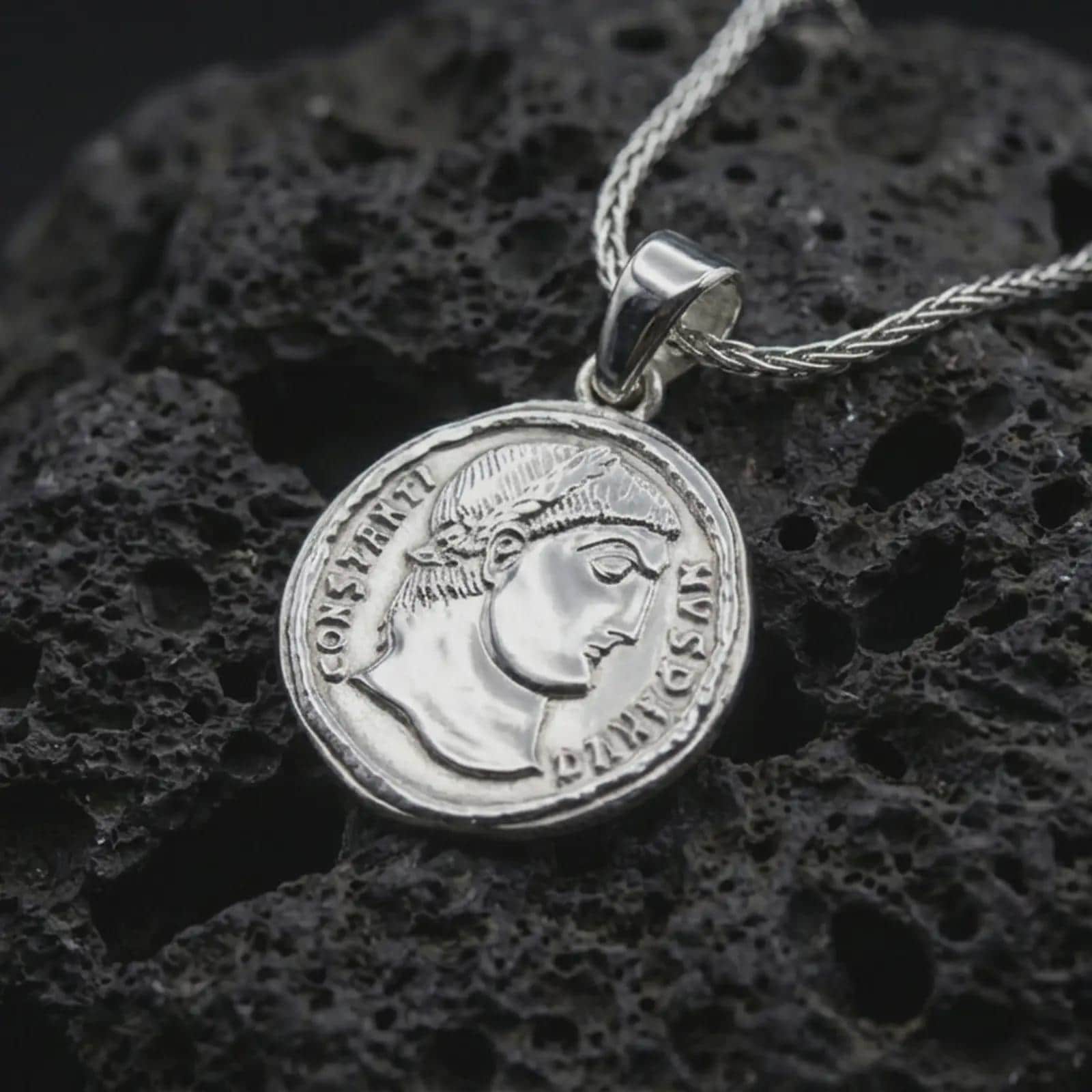 Polished silver Emperor Constans coin pendant necklace displayed on dark volcanic rock, shown in a premium close-up image that highlights the classical emperor portrait and ancient Roman coin texture.