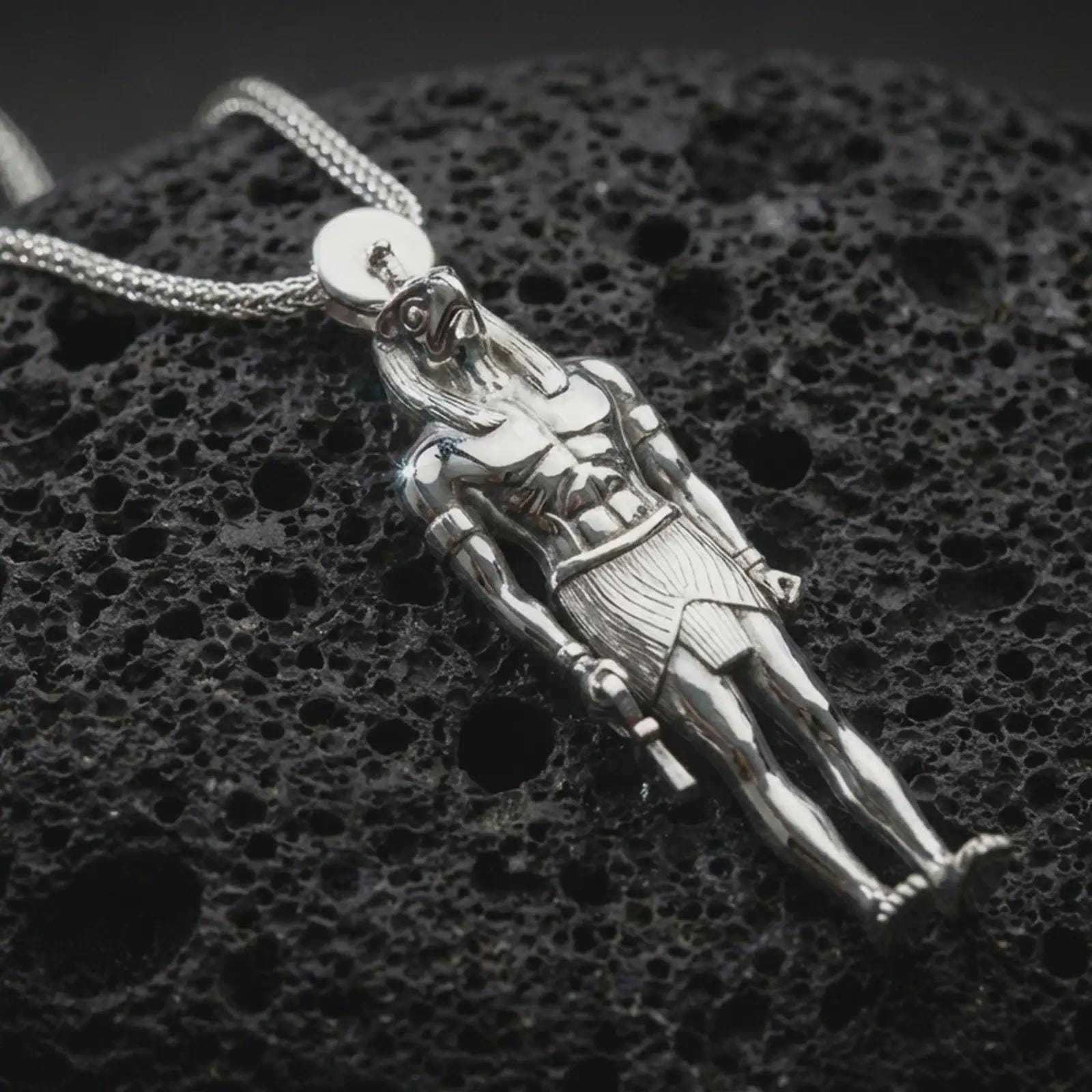 Polished silver Ra amulet pendant necklace displayed on dark volcanic rock, shown in a premium close-up image that highlights the Egyptian god figure, muscular relief, and elongated ceremonial silhouette.
