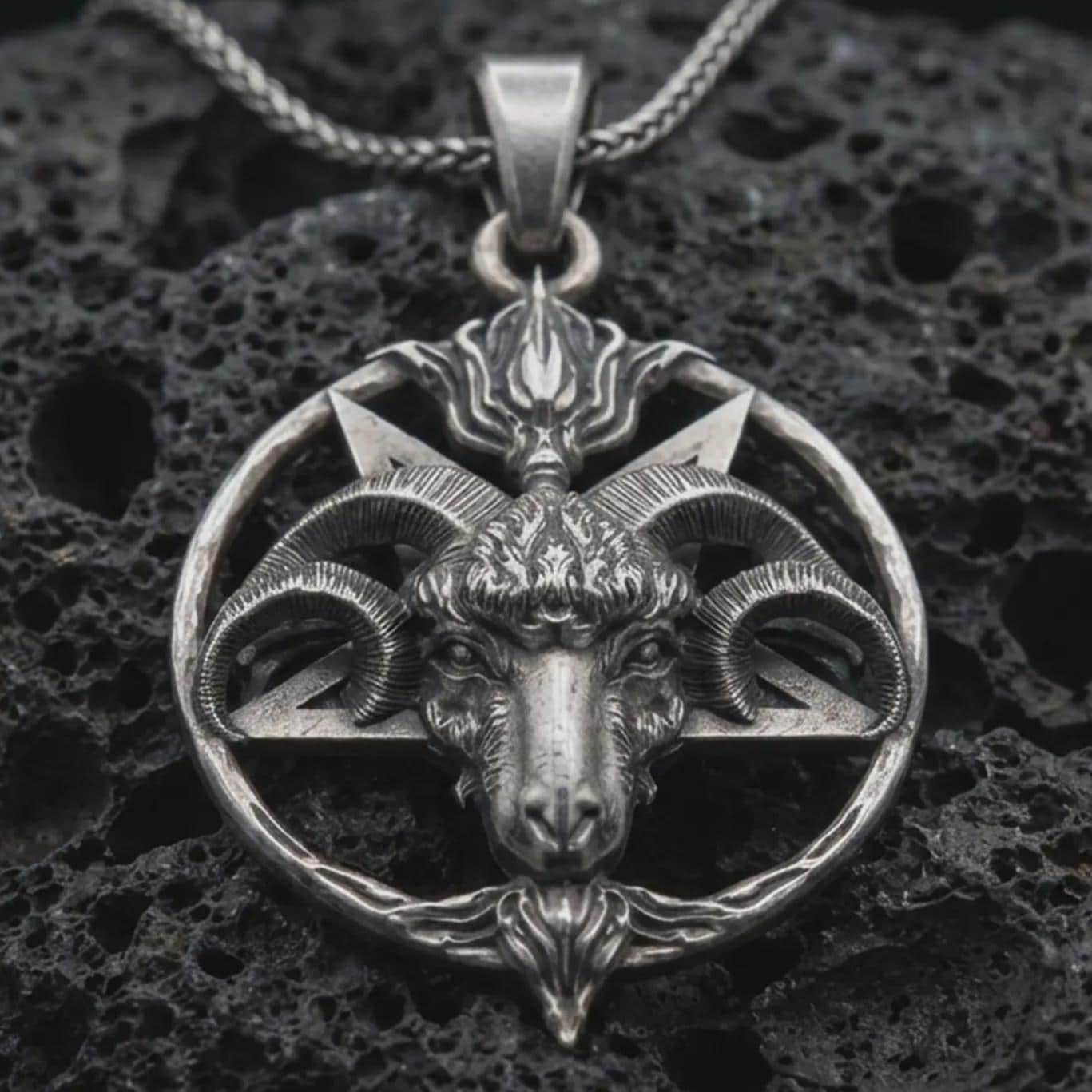 Sterling silver Baphomet goat head pendant necklace with an oxidized finish resting on textured volcanic rock, captured in a close-up premium studio composition.
