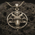 Load image into Gallery viewer, Bronze Baphomet goat head pendant necklace with an oxidized finish resting on textured volcanic rock, captured in a close-up premium studio composition.
