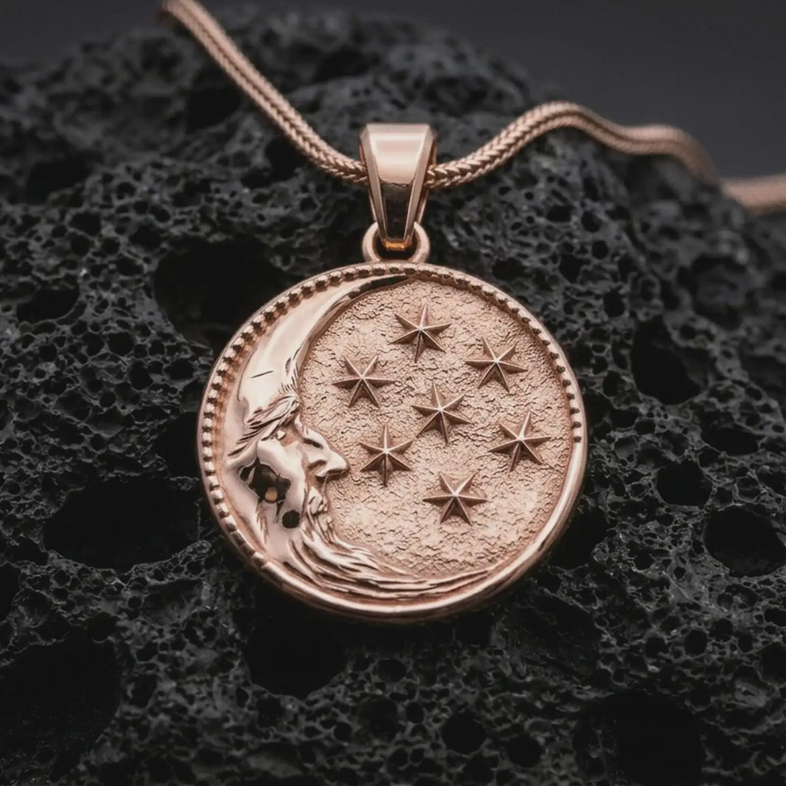Rose gold plated moon and stars pendant necklace on dark volcanic rock, photographed in a detailed premium studio macro view.