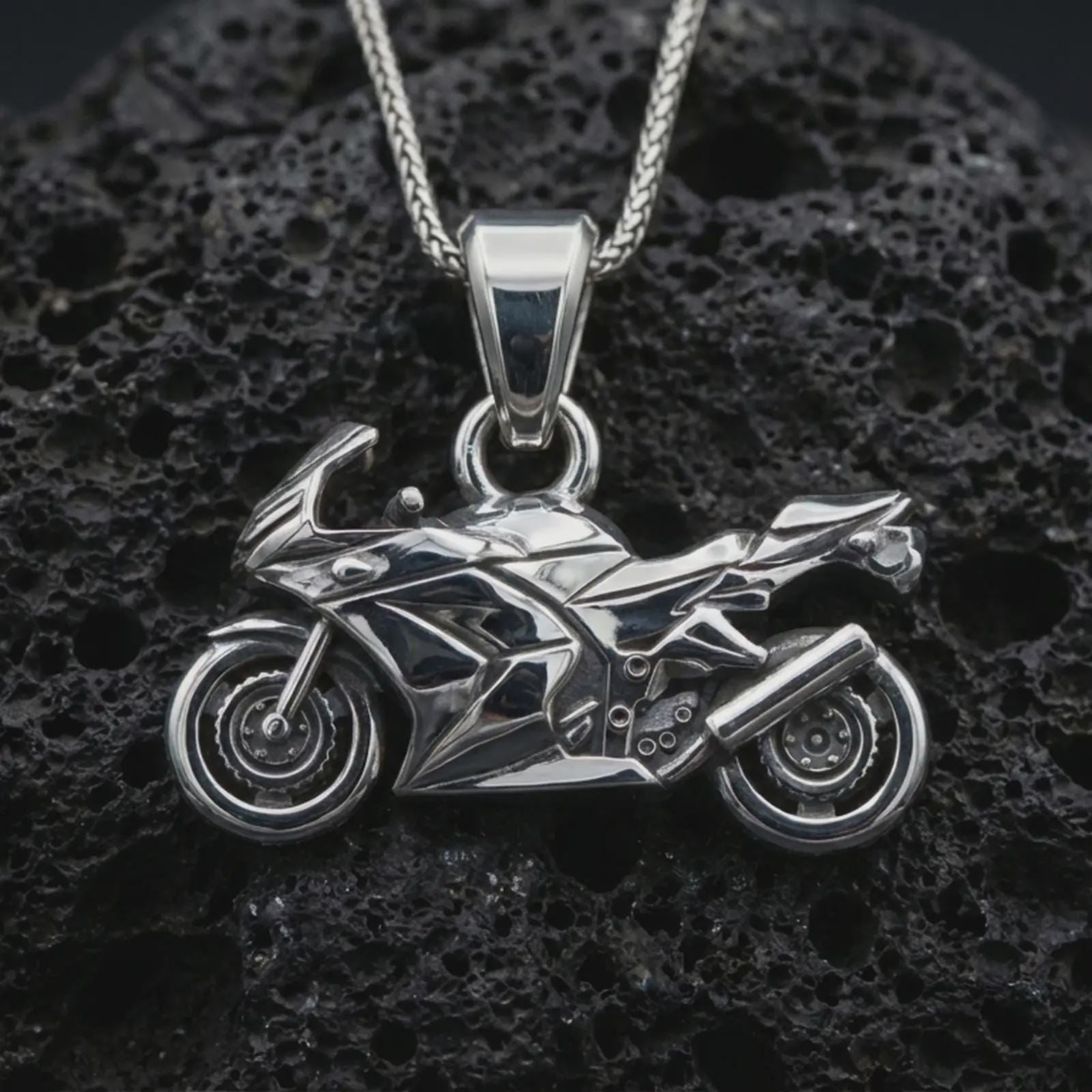 Polished silver sportbike motorcycle pendant necklace displayed on black volcanic rock, shown in a refined macro product shot with angular fairing, wheel, and exhaust detail.