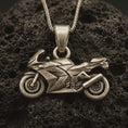 Load image into Gallery viewer, Bronze sportbike motorcycle pendant necklace with an oxidized finish resting on textured volcanic rock, captured in a close-up premium studio composition.
