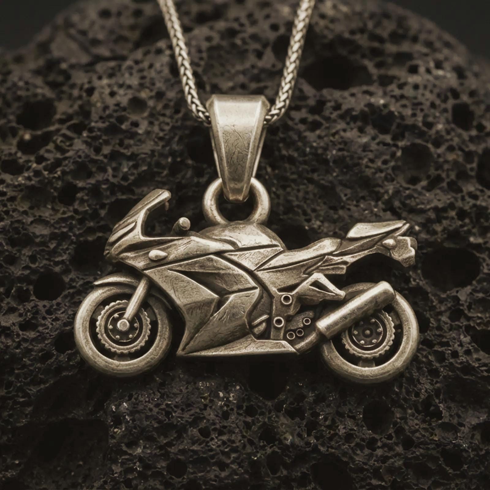 Bronze sportbike motorcycle pendant necklace with an oxidized finish resting on textured volcanic rock, captured in a close-up premium studio composition.
