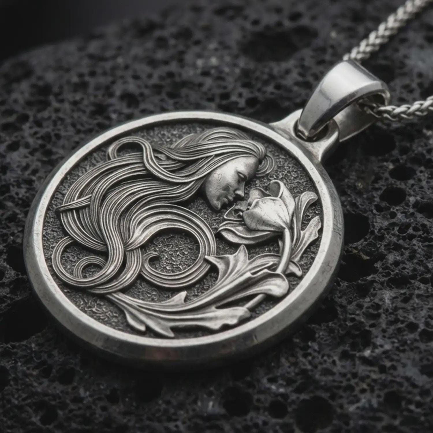 Sterling silver Art Nouveau woman pendant necklace with an oxidized finish resting on textured volcanic rock, captured in a close-up premium studio composition.