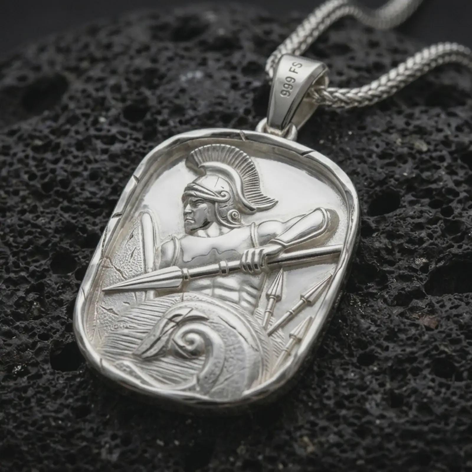 Polished silver Roman soldier pendant necklace displayed on black volcanic rock, shown in a refined macro product shot with detailed helmet, spear, shield, and wave relief.