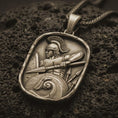 Load image into Gallery viewer, Bronze Roman soldier pendant necklace with an oxidized finish resting on textured volcanic rock, captured in a close-up premium studio composition.
