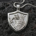 Load image into Gallery viewer, Polished silver samurai shield pendant necklace displayed on black volcanic rock, shown in a refined macro product shot with detailed armored warrior, sword, wooden shield, and arrow quiver relief.

