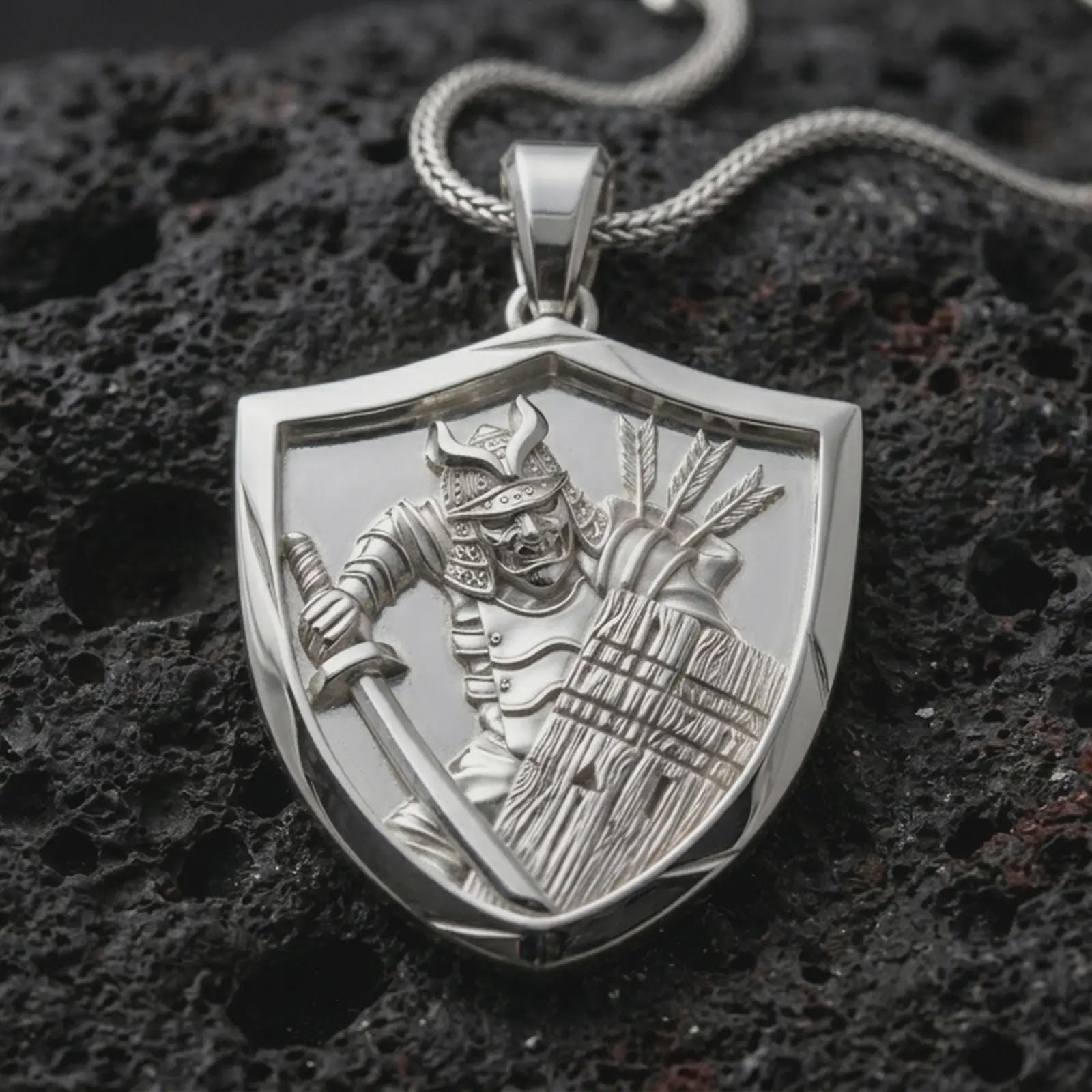 Polished silver samurai shield pendant necklace displayed on black volcanic rock, shown in a refined macro product shot with detailed armored warrior, sword, wooden shield, and arrow quiver relief.