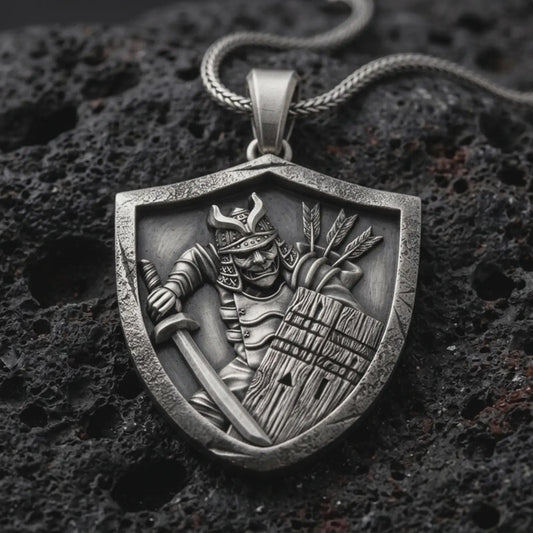 Sterling silver samurai shield pendant necklace with an oxidized finish resting on textured volcanic rock, captured in a close-up premium studio composition.