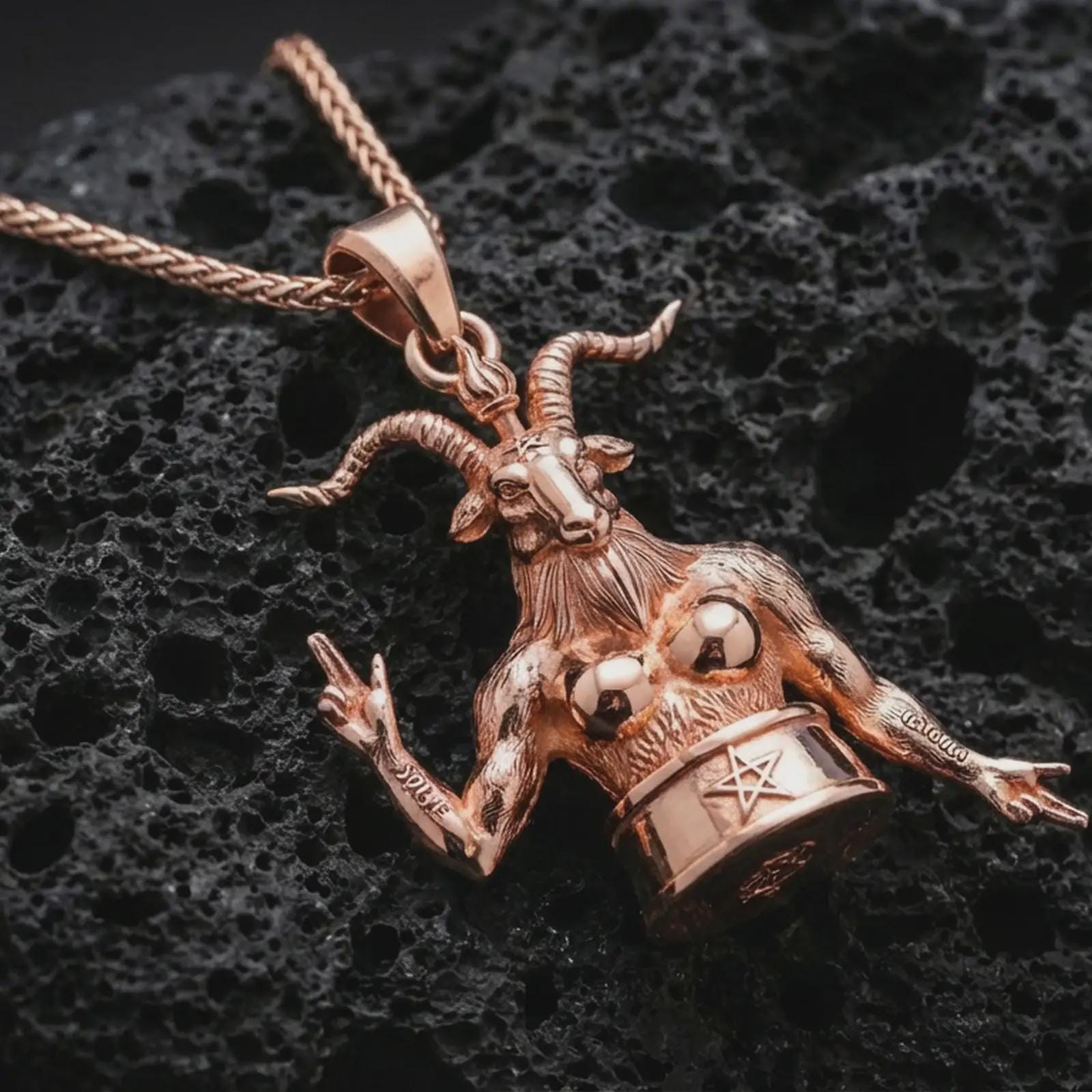 Rose gold plated Baphomet pendant necklace on dark volcanic rock, photographed in a detailed premium studio macro view.
