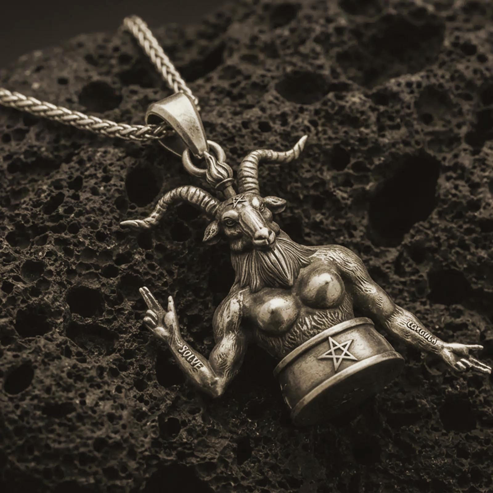 Bronze Baphomet pendant necklace with an oxidized finish resting on textured volcanic rock, captured in a close-up premium studio composition.