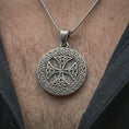 Load image into Gallery viewer, Oxidized Celtic knot medallion necklace worn on the neck, styled in a dark lifestyle portrait with an open shirt and masculine presentation.
