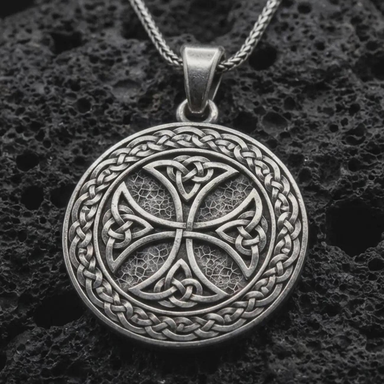 Sterling silver Celtic knot medallion necklace with an oxidized finish resting on textured volcanic rock, captured in a close-up premium studio composition.