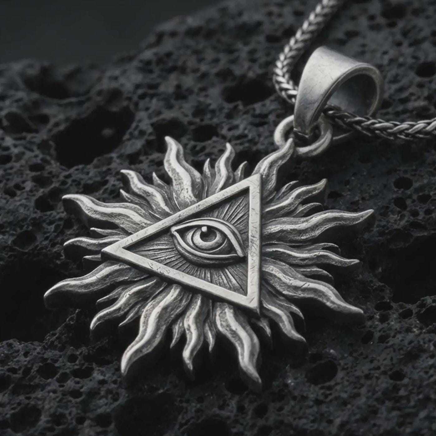 Sterling silver Eye of Providence sun pendant necklace with an oxidized finish resting on textured volcanic rock, captured in a close-up premium studio composition.