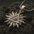 Load image into Gallery viewer, Bronze Eye of Providence sun pendant necklace with an oxidized finish resting on textured volcanic rock, captured in a close-up premium studio composition.
