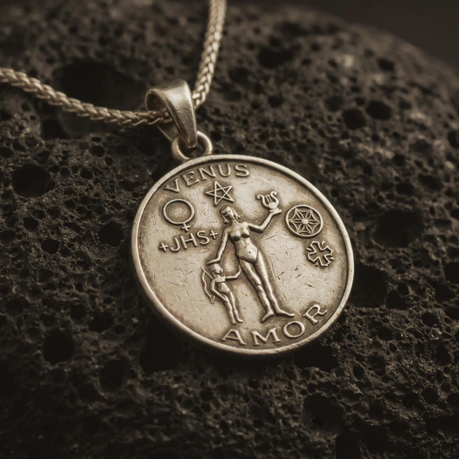 Bronze Venus Amor pendant necklace with an oxidized finish resting on textured volcanic rock, captured in a close-up premium studio composition.