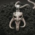 Load image into Gallery viewer, Polished silver Mythosaur skull pendant necklace displayed on black volcanic rock, shown in a refined macro product shot with horned alien skull detail and rugged sci-fi relief.
