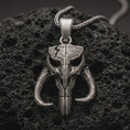 Load image into Gallery viewer, Sterling silver Mythosaur skull pendant necklace with an oxidized finish resting on textured volcanic rock, captured in a close-up premium studio composition.
