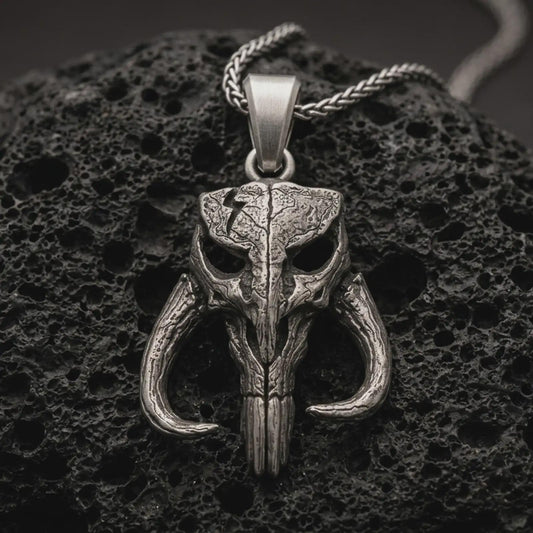 Sterling silver Mythosaur skull pendant necklace with an oxidized finish resting on textured volcanic rock, captured in a close-up premium studio composition.