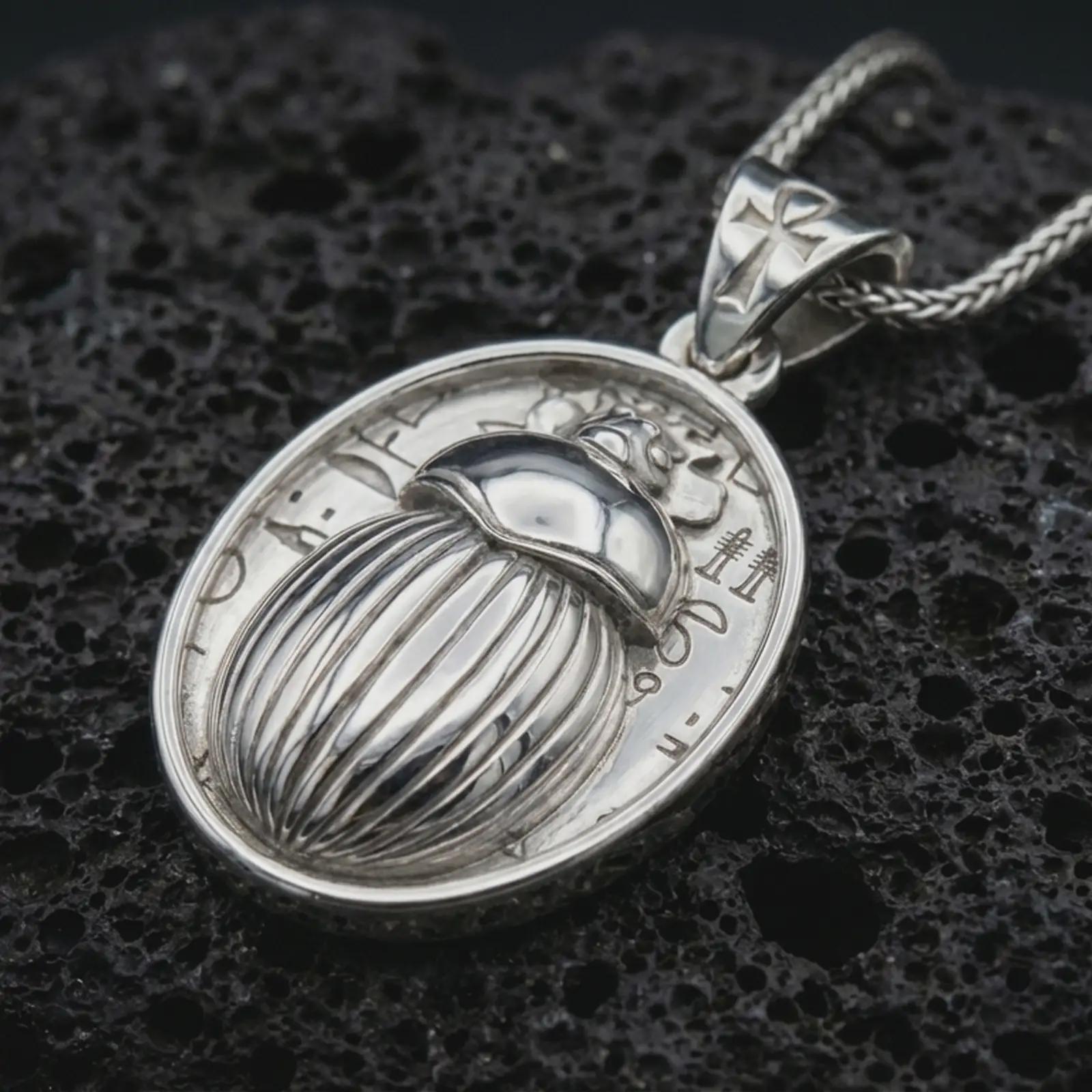 Polished silver Egyptian scarab pendant necklace displayed on black volcanic rock, shown in a refined macro product shot with carved beetle relief, symbolic hieroglyph details, and ankh-inspired bail.