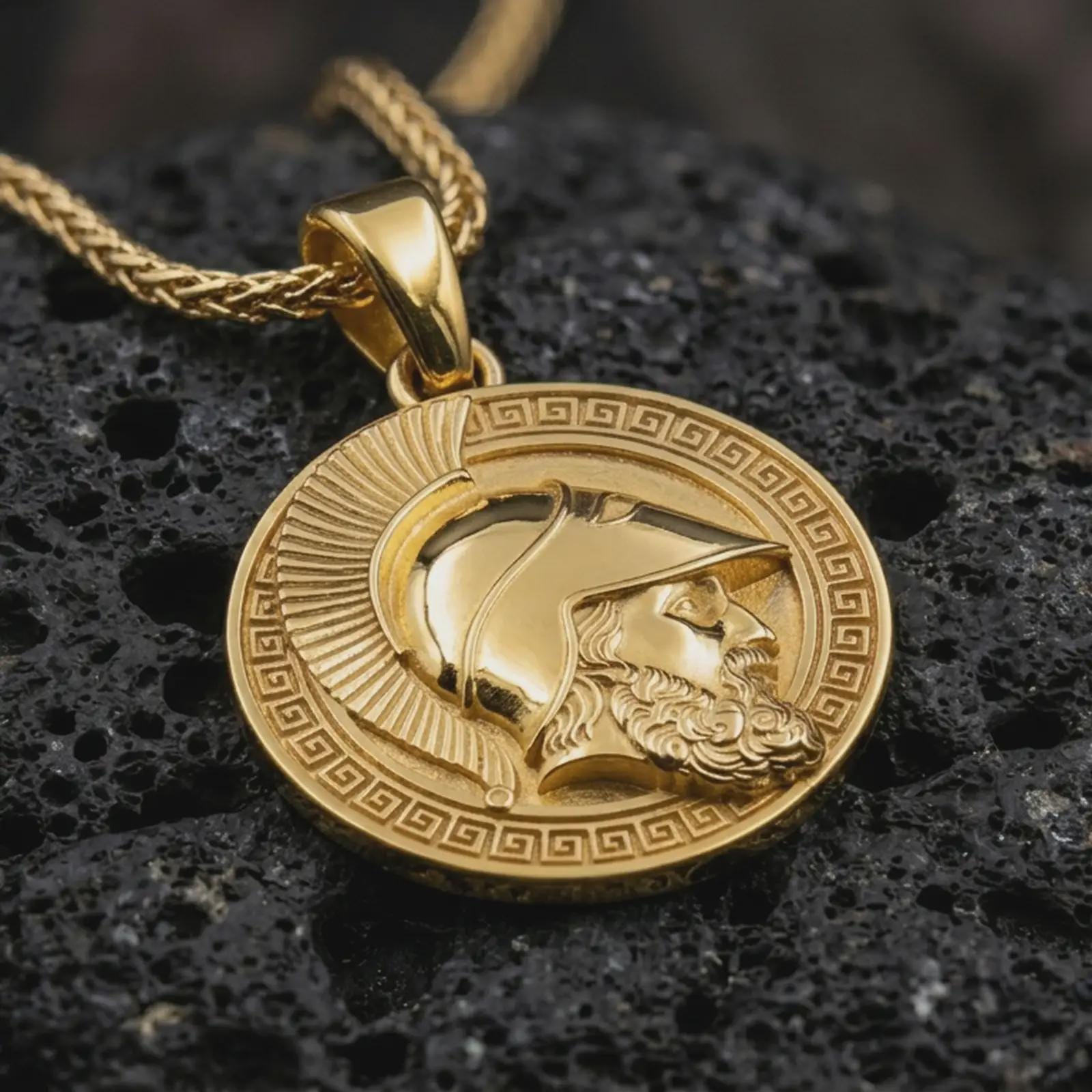 Gold plated Spartan helmet pendant necklace presented on porous volcanic rock, highlighting the ancient Greek warrior medallion design in a luxurious close-up jewelry image.