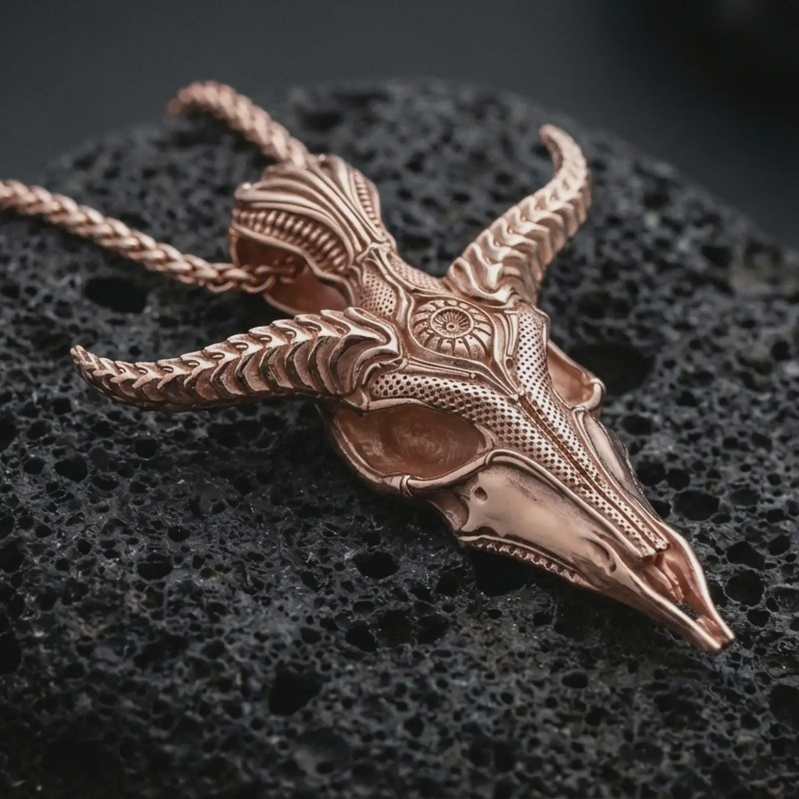 Rose gold plated Baphomet skull pendant necklace on dark volcanic rock, photographed in a detailed premium studio macro view.