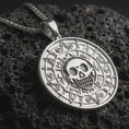 Load image into Gallery viewer, Polished silver cursed Aztec coin pendant necklace displayed on black volcanic rock, shown in a refined macro product shot with pirate skull center and circular symbolic pattern.
