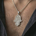 Load image into Gallery viewer, Polished silver Jerusalem Hamsa hand pendant necklace worn on the neck, shown against the chest in a clean and symbolic everyday wear composition.
