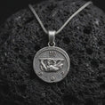 Load image into Gallery viewer, Oxidized Emperor Augustus coin pendant necklace resting on black volcanic stone, featuring a Roman imperial side profile with laurel wreath and engraved ancient lettering in a detailed macro product photograph.
