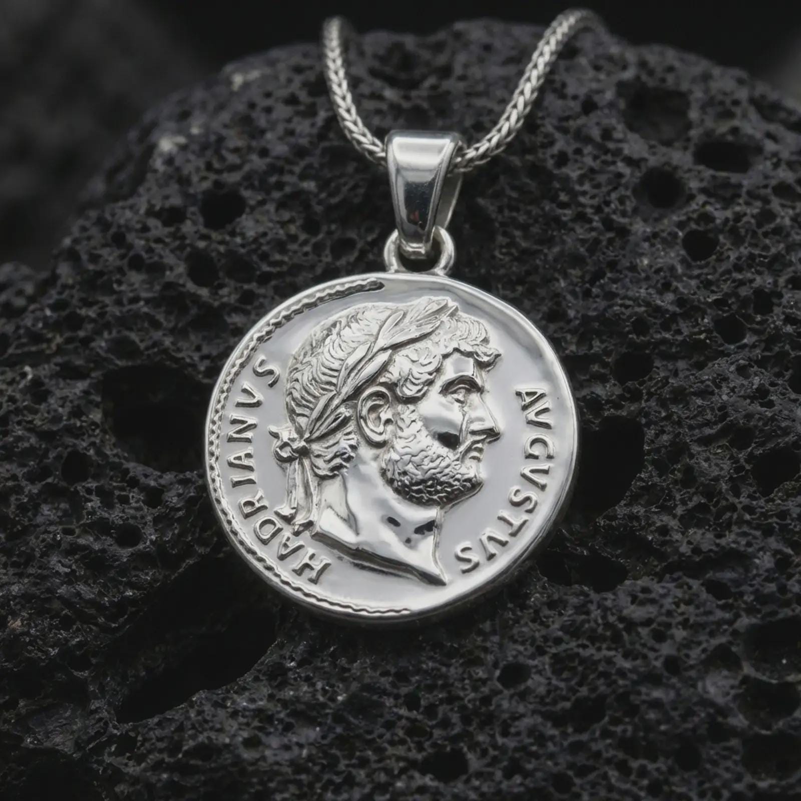 Polished silver Emperor Augustus coin pendant necklace displayed on dark volcanic rock, shown in a premium close-up image that highlights the classical emperor portrait and antique Roman coin texture.