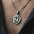 Load image into Gallery viewer, Oxidized Janus coin pendant necklace worn on the neck, styled in a dark lifestyle image that presents the ancient Roman god motif as a bold symbolic and historical statement piece.
