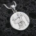 Load image into Gallery viewer, Polished silver Alexander the Great coin pendant necklace displayed on dark volcanic rock, shown in a premium close-up image that highlights the antique medallion texture, heroic figure, and historical Greek inscription.

