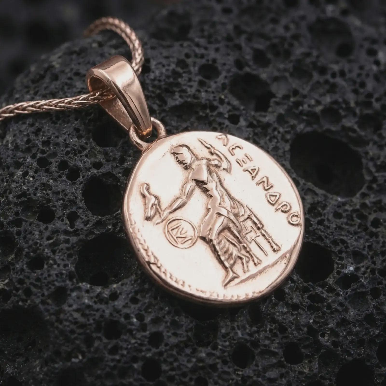 Rose gold plated Alexander the Great coin pendant necklace presented on textured volcanic stone, showcasing the engraved Greek figure, antique-inspired surface, and round historic medallion form in a macro studio shot.