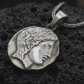 Load image into Gallery viewer, Oxidized ancient Greek coin pendant necklace resting on black volcanic stone, featuring a classical female profile in an irregular coin-shaped relief with antique-inspired surface texture.

